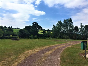 A gravel track across the mown grass field, with wooded hills beyond