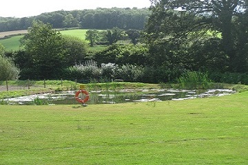A pond with a lifebuoy beside the mown grass, with fields beyond